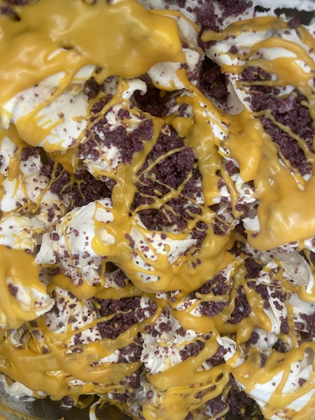 Primo piano di gelato bianco cremoso con briciole di biscotto al cacao e colate di salsa gialla lucida